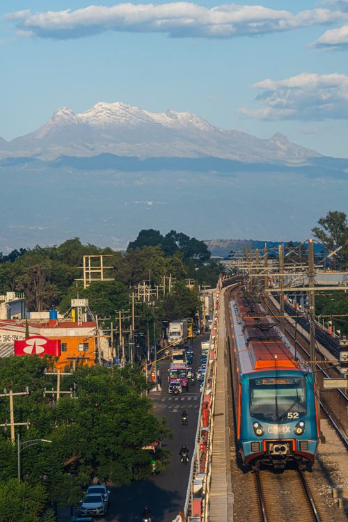 Free A train travels through a Mexican city with a mountain range in the background, under a bright sky. Stock Photo