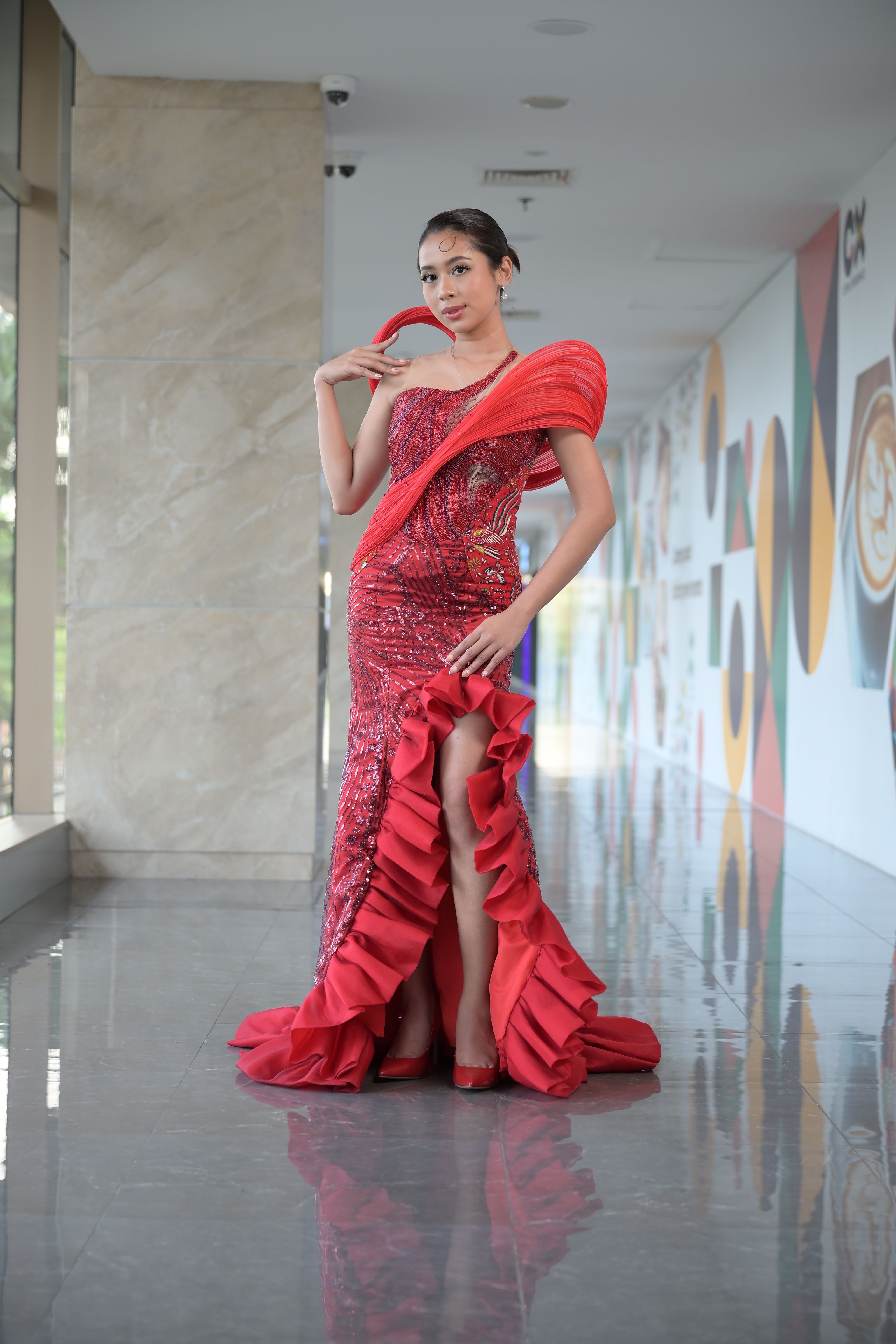 Mulher elegante posando em um glamoroso vestido vermelho em um ambiente interno moderno.
