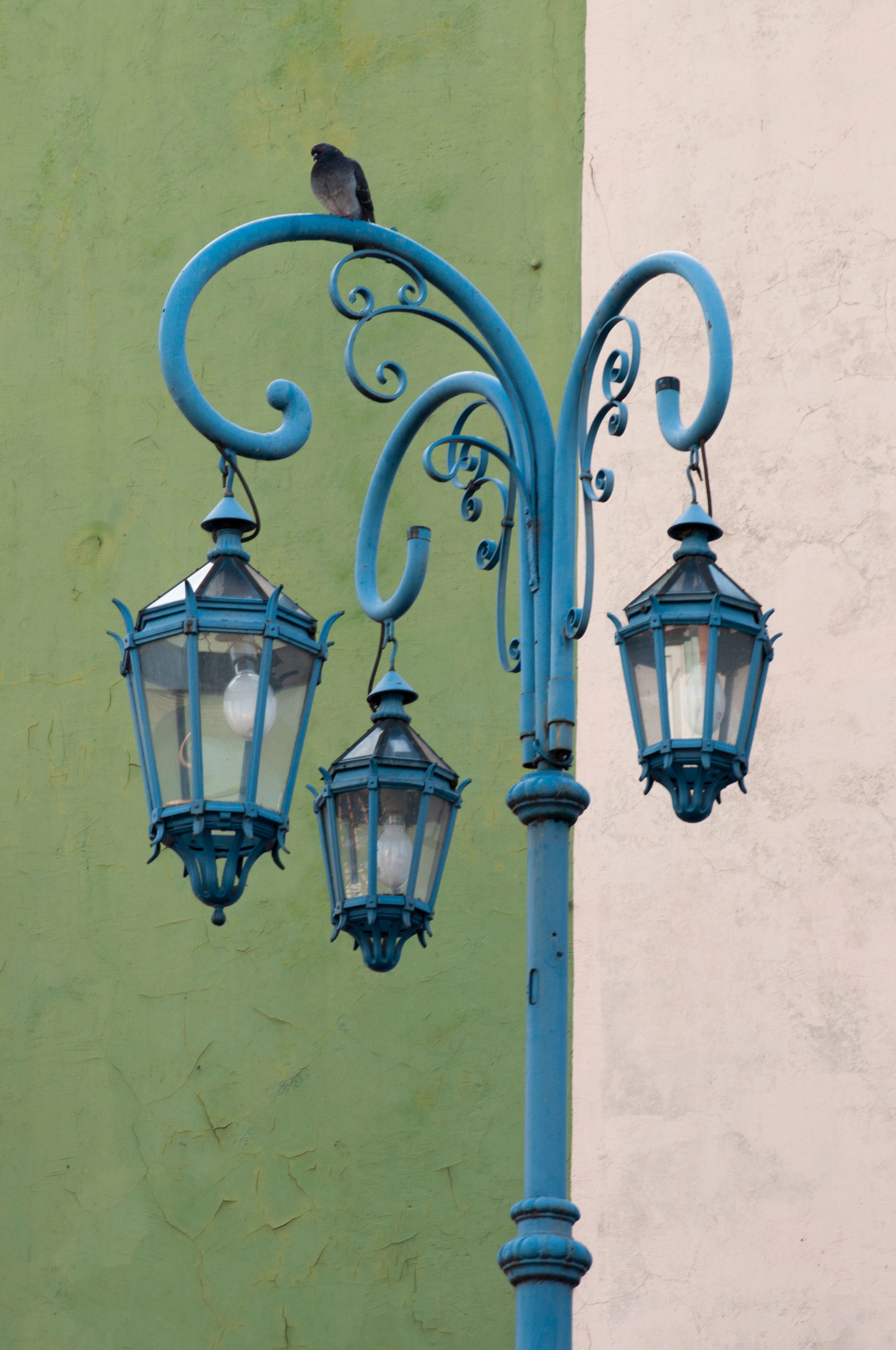 A decorative street lantern with a bird perched on top, set against a pastel wall.