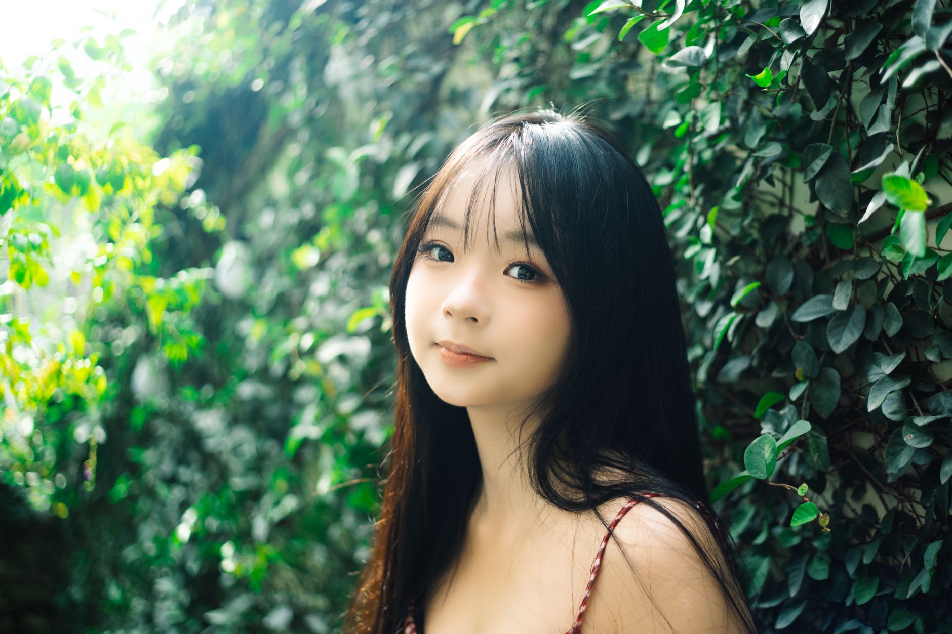 Portrait of a young woman surrounded by lush green foliage creating a tranquil and natural atmosphere.
