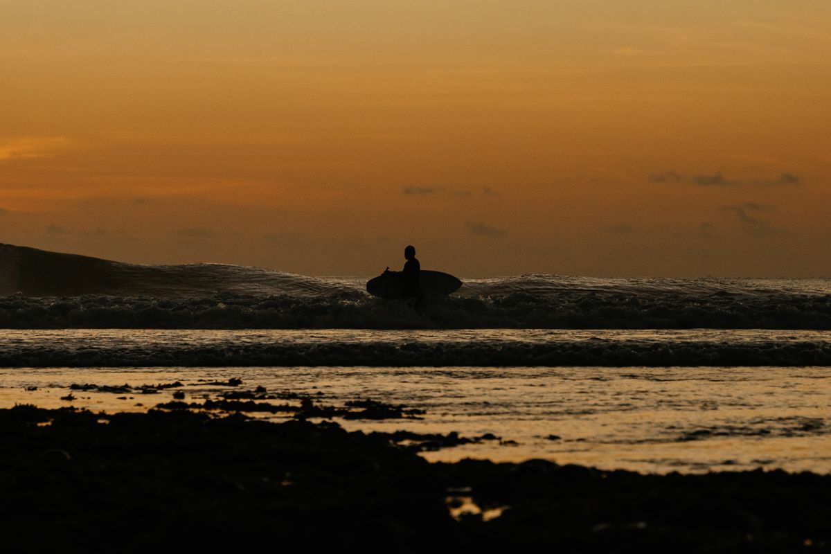 Surfer carrying a board at sunset