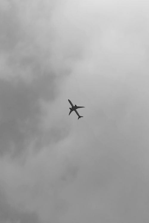Free Black and white image of an airplane flying through a cloudy sky, emphasizing minimalism. Stock Photo