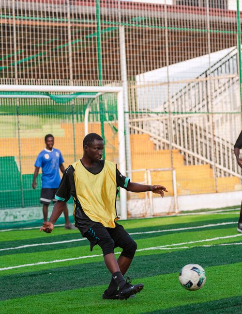 Free A group of teenagers playing soccer on an outdoor field, focusing on a player in a yellow vest. Stock Photo