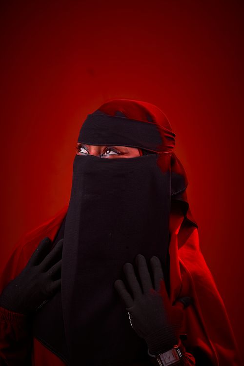 Free Portrait of a woman in traditional veiled attire against a vivid red backdrop. Stock Photo