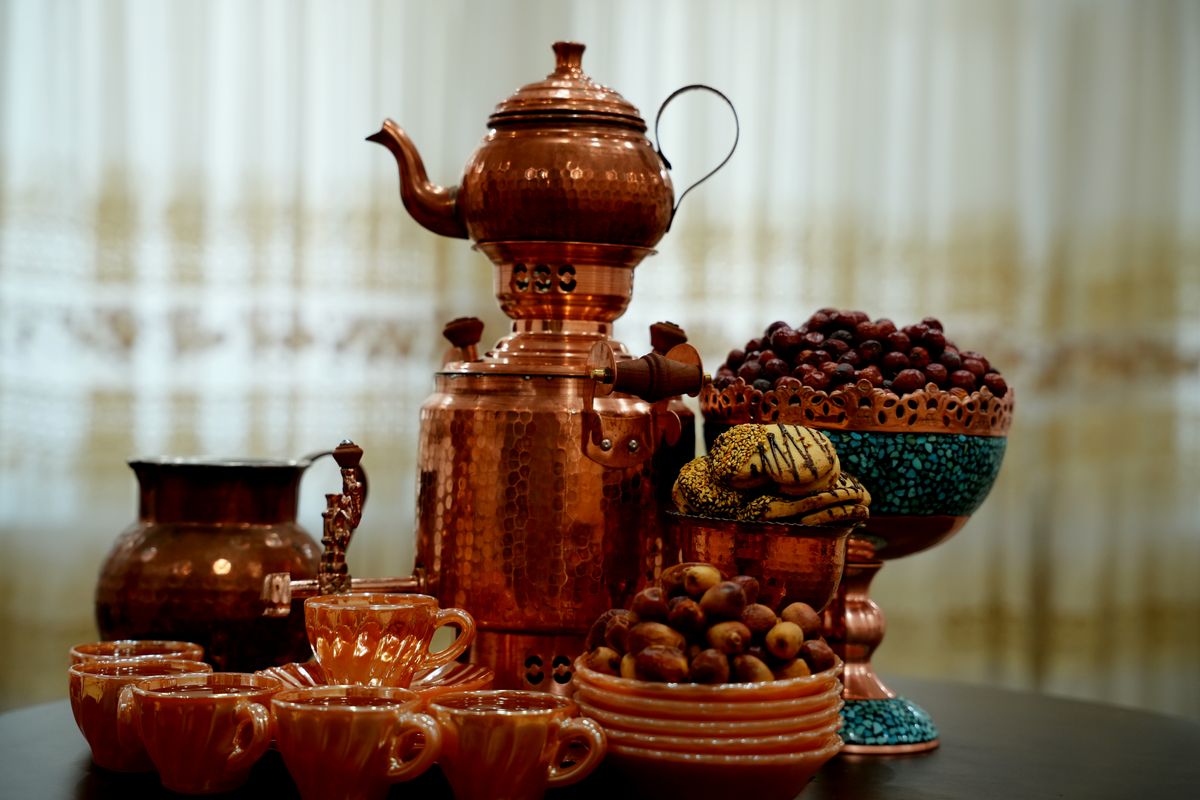 A beautifully arranged copper tea set with a samovar, cups, and bowls filled with dates and sweets.