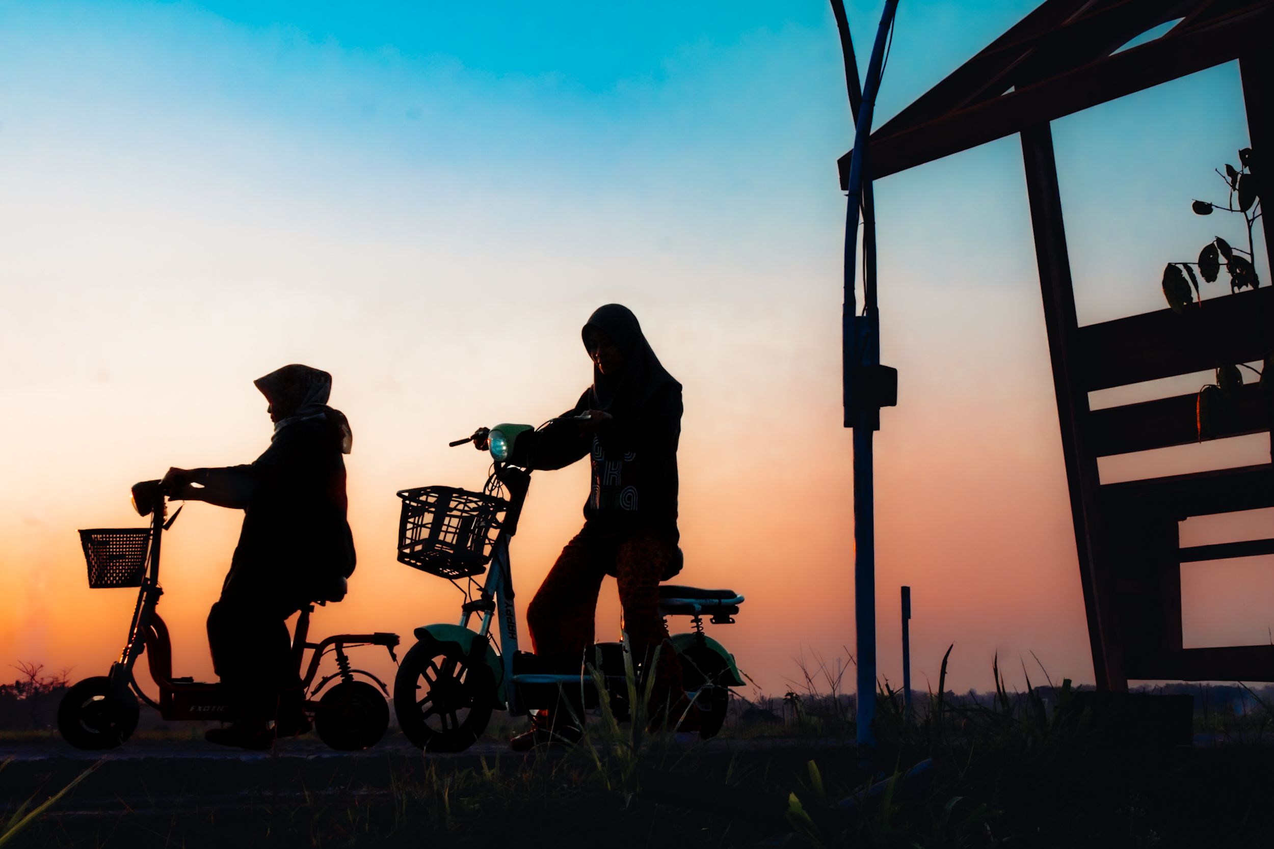 Two women silhouetted on electric scooters against a vibrant sunset in Jogja.