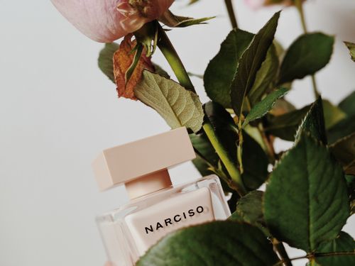 Free Stylish perfume bottle with a pink flower and green leaves, creating a fresh and elegant aesthetic. Stock Photo