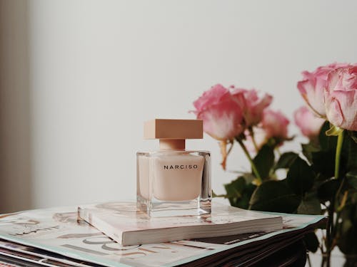 Free Sophisticated Narciso perfume bottle with pink roses and magazines. Perfect for elegance and fragrance themes. Stock Photo