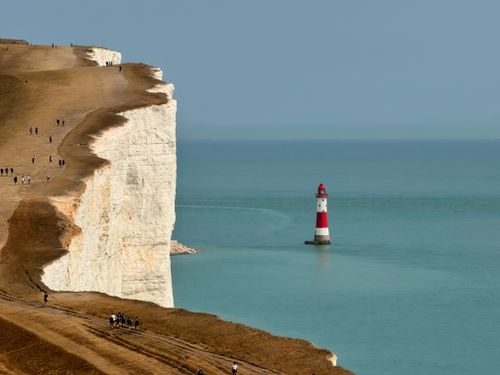 Free Stunning view of the Beachy Head cliffs and lighthouse in England with people walking along the cliff edge. Stock Photo