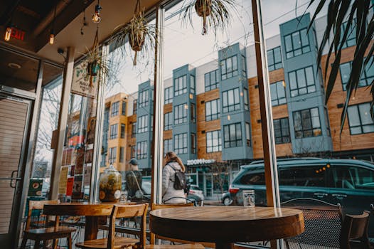 这家咖啡馆内部温暖舒适，配有木制家具，透过大窗户可以欣赏到现代城市建筑的景色