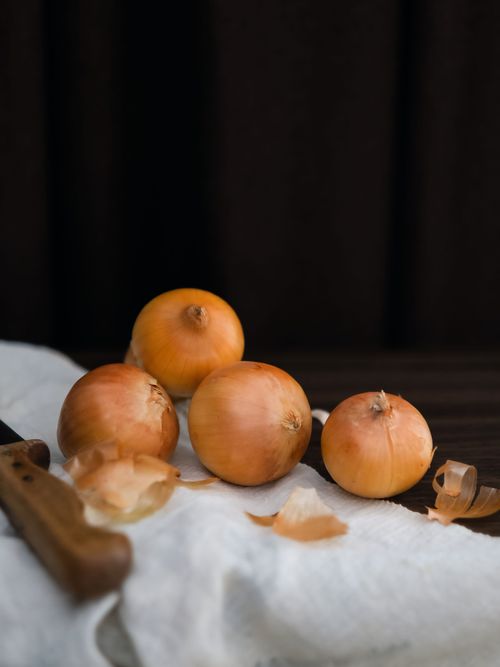 Free A group of fresh yellow onions with a knife on a white cloth surface. Stock Photo
