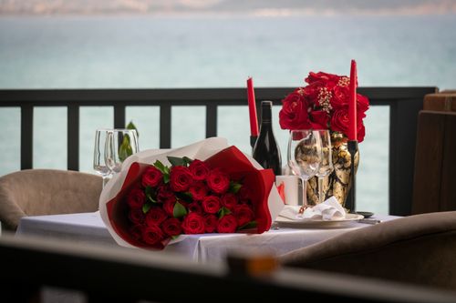 Free Elegant seaside dinner setup with red roses, wine, and candlelit ambiance, perfect for romance. Stock Photo