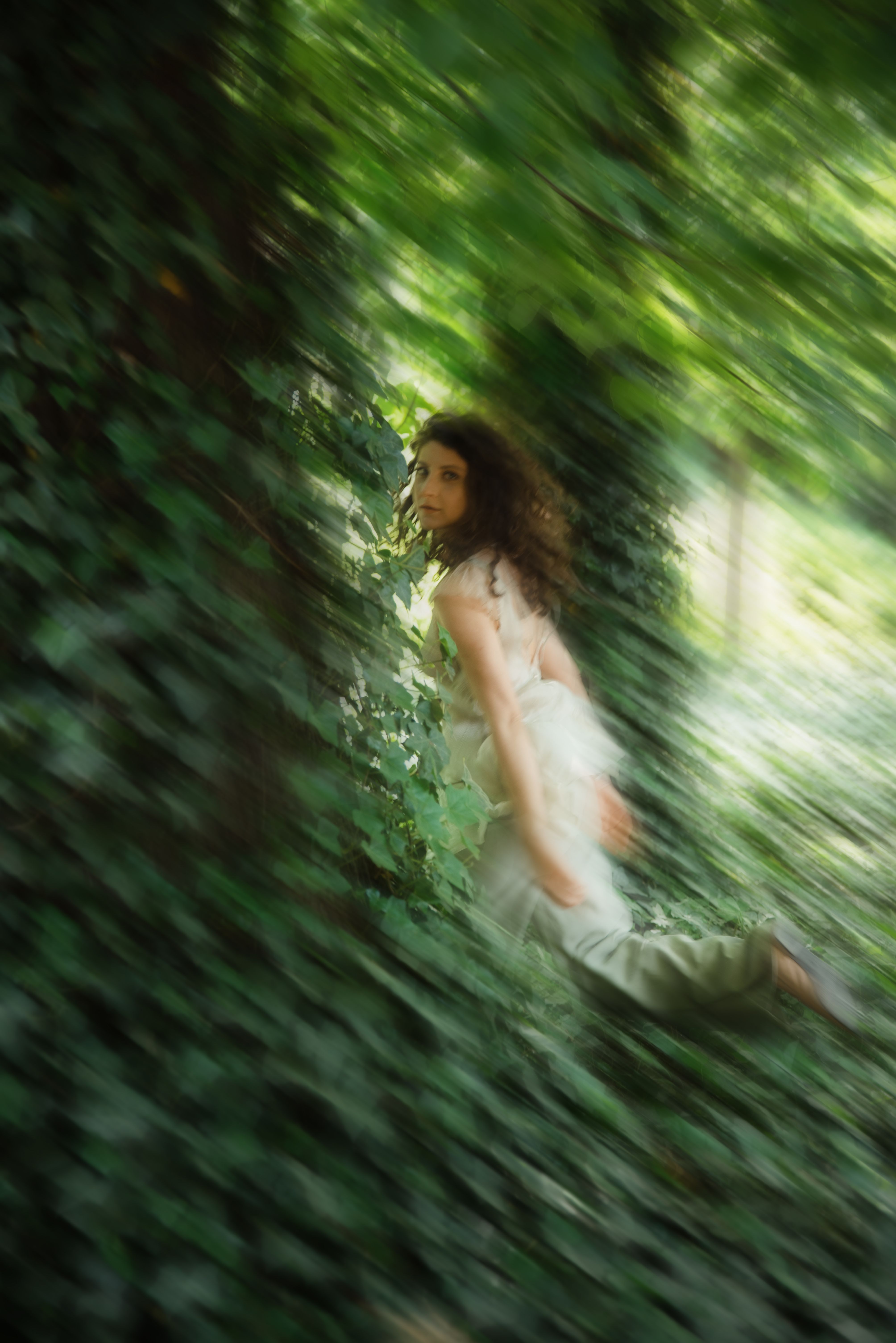 Blurred motion of a woman amidst green foliage, conveying a sense of mystery and enchantment.
