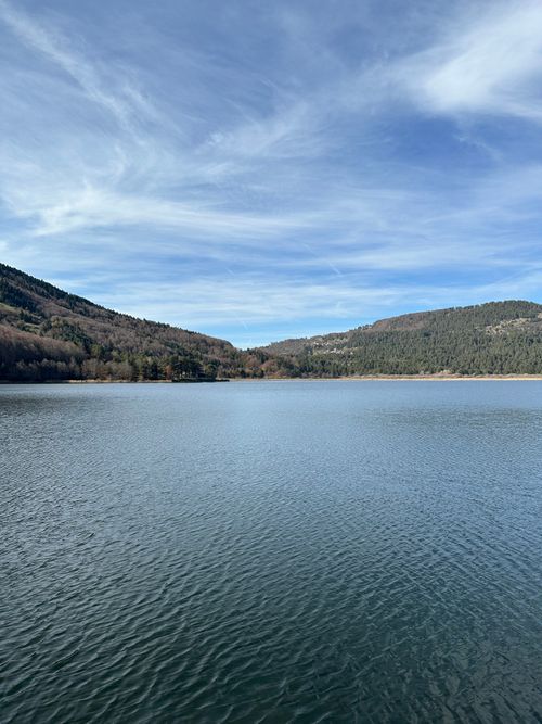 Free Calm lake with surrounding mountains under a clear blue sky, offering a peaceful nature scene. Stock Photo