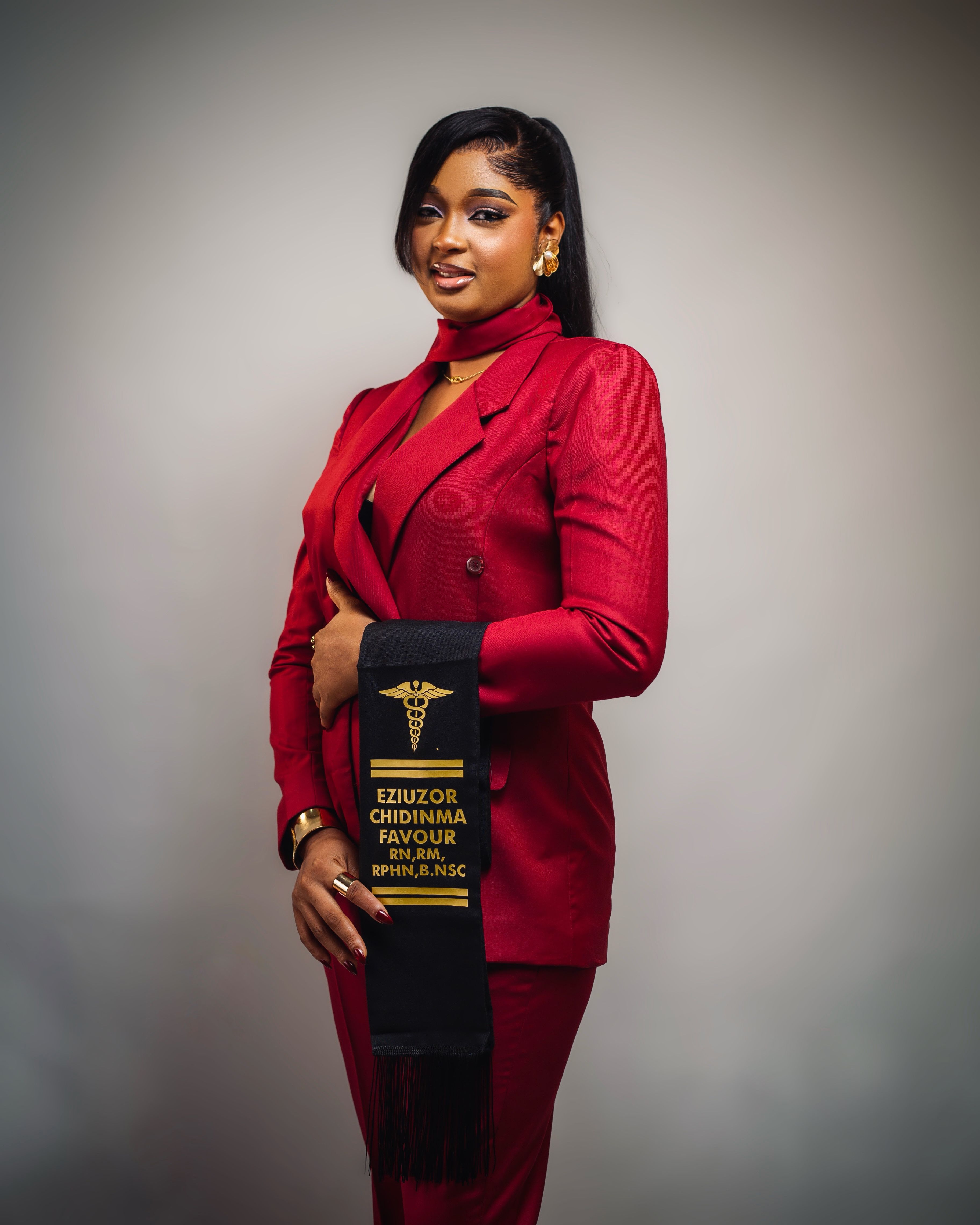 Elegant portrait of a professional woman in red formal attire holding a graduation stole.