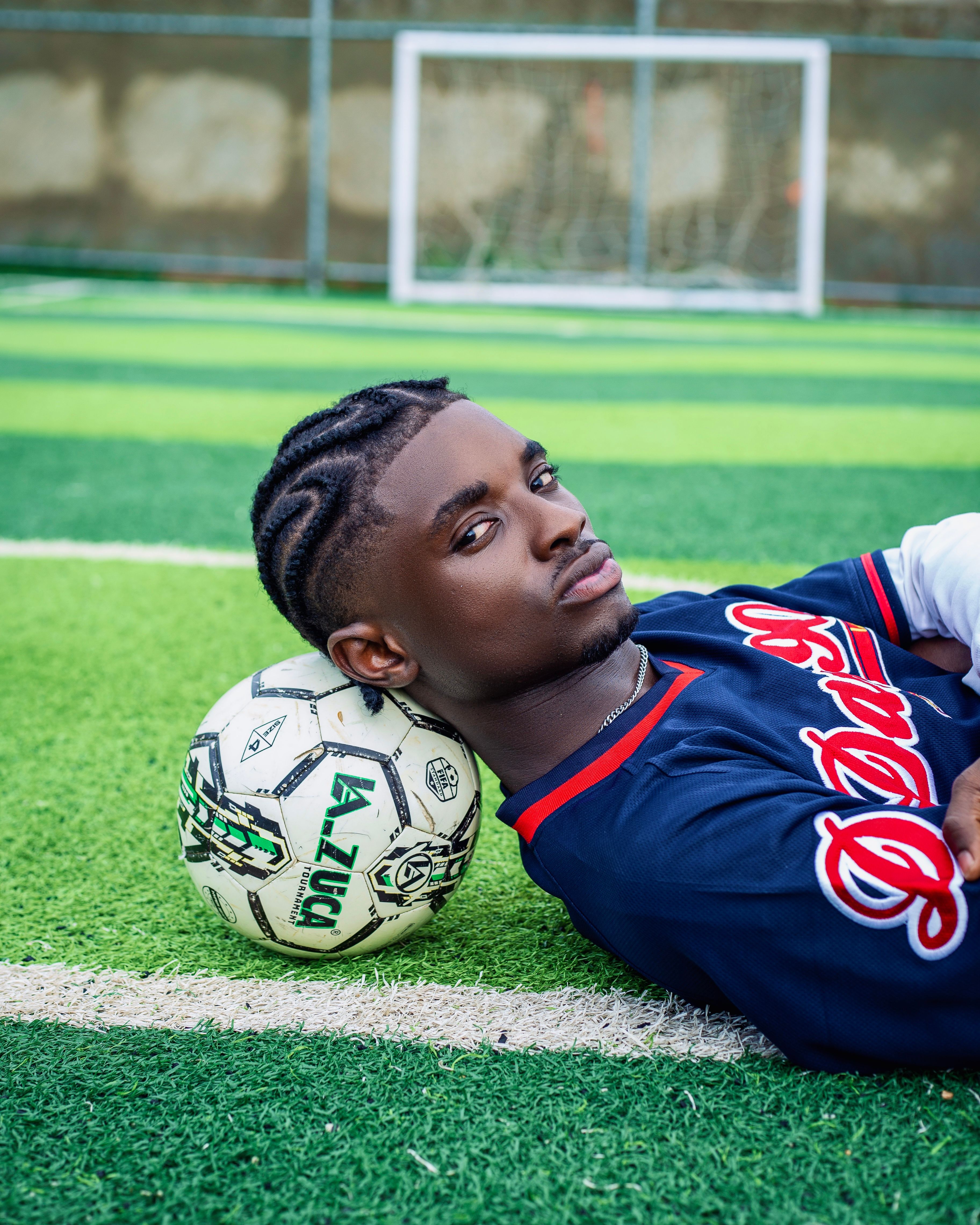 Young man with a soccer ball on a green field in Kano, Nigeria