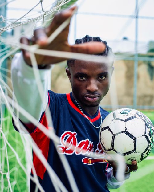 Free Focused young African soccer player posing with ball in goal net, emphasizing sports passion. Stock Photo