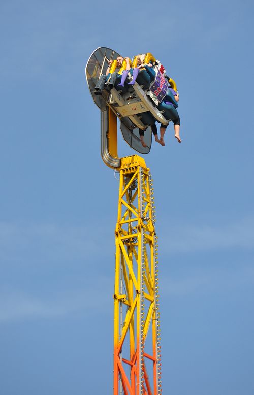 Free Adventurous people enjoying a thrilling vertical ride on a sunny day at an amusement park. Stock Photo