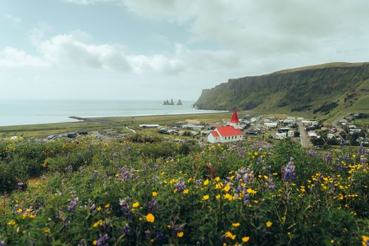 Idyllic landscape of Vík í Mýrdal with a red-roofed church and ocean view.