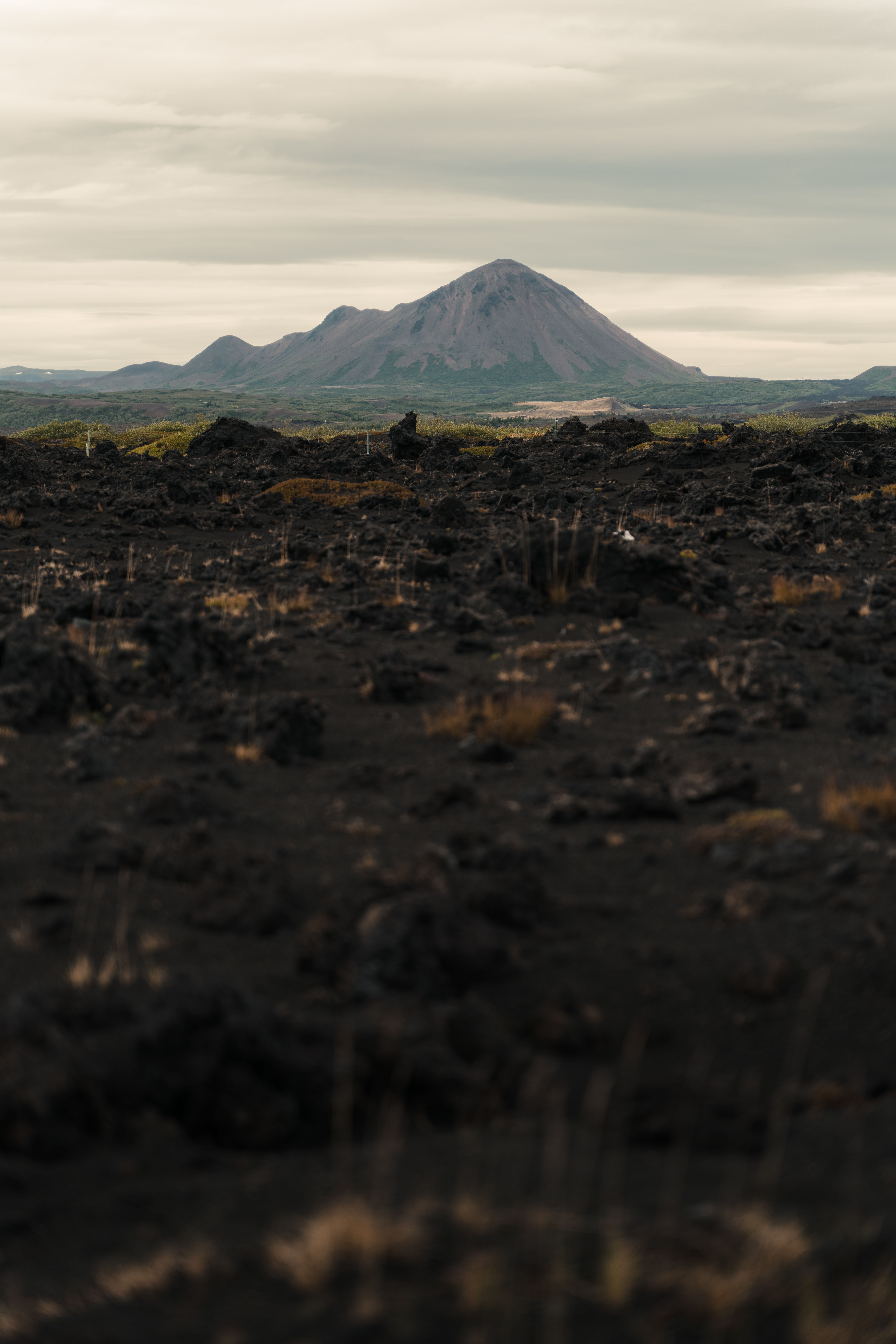 Dramatic volcanic terrain with distant view of a mountain under cloudy skies.