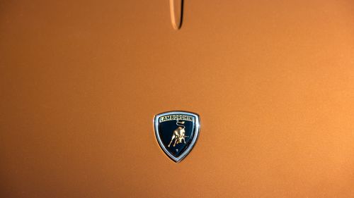 Free Close-up of Lamborghini emblem on sleek orange car hood. Stock Photo