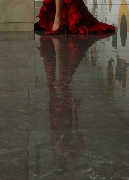 Free Reflection of a woman in a red dress on a polished marble floor creating a striking visual effect. Stock Photo