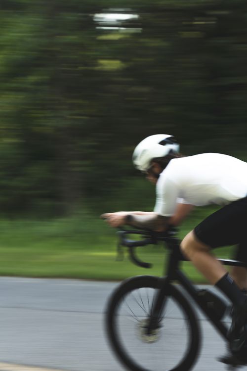 Free Blurred motion of a cyclist racing down a road amid lush greenery, capturing speed and athleticism. Stock Photo