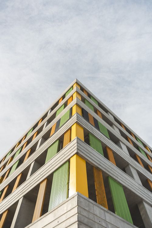 Free A modern building featuring a vibrant facade with yellow, green, and orange elements against a cloudy sky. Stock Photo
