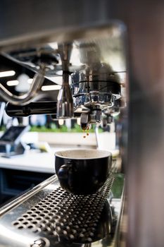 Detailed view of espresso dripping into a cup from a professional coffee machine.