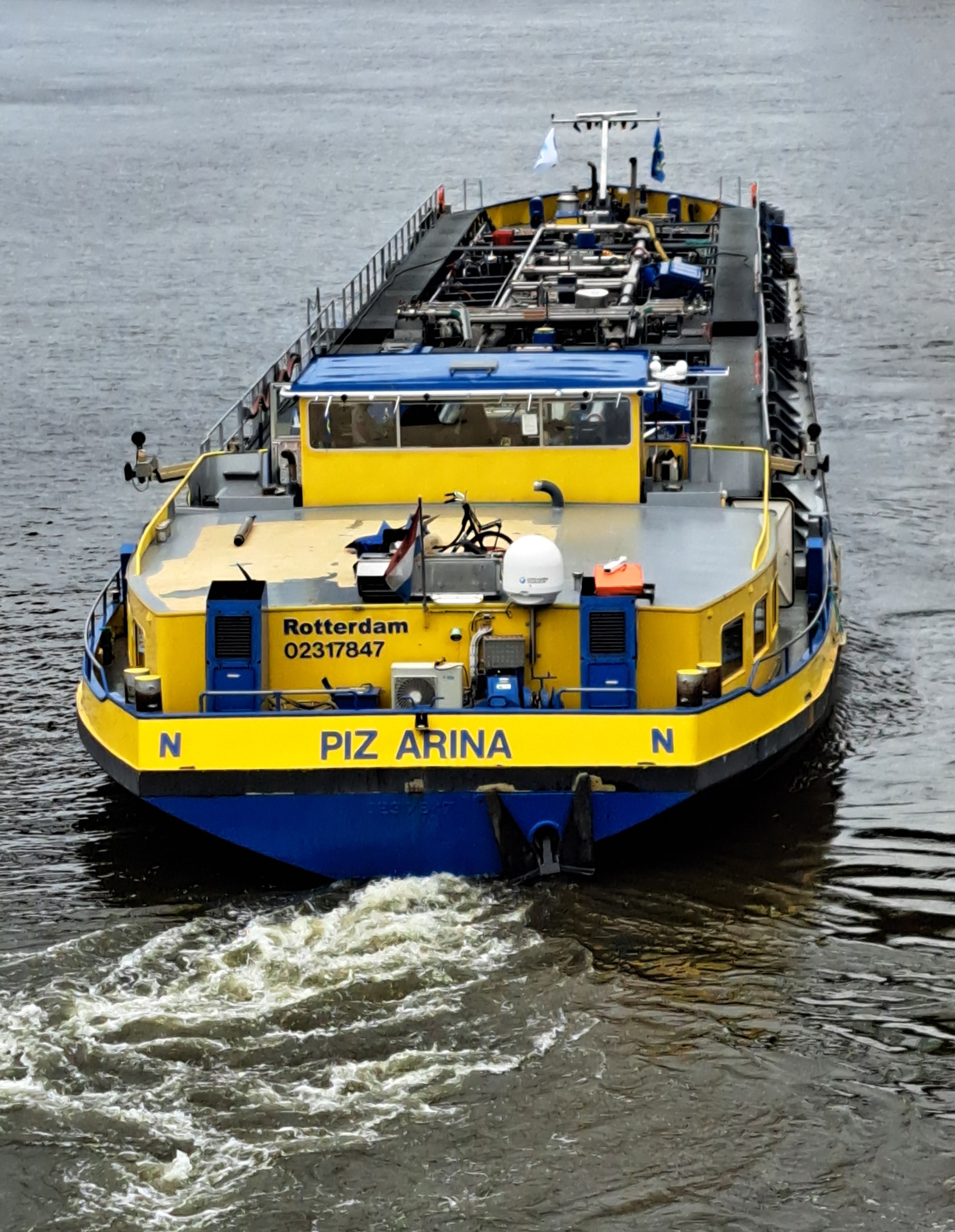 A yellow and blue cargo ship named PIZ ARINA navigating the waters of Rotterdam.