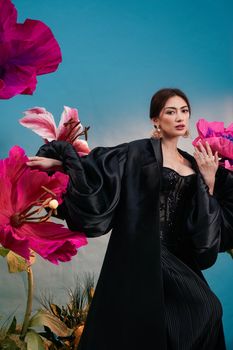 Fashionable woman in black attire amidst oversized vibrant flowers.