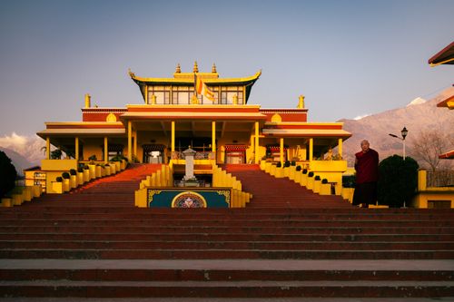 Free Golden sunlight illuminates a Buddhist temple in Sidhbari, with a monk standing nearby, creating a serene atmosphere. Stock Photo