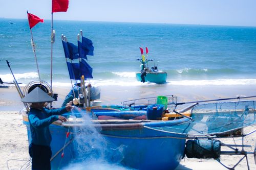 Free Fishermen in Vietnam preparing traditional boats on the beach under sunny skies, capturing local culture and ocean life. Stock Photo