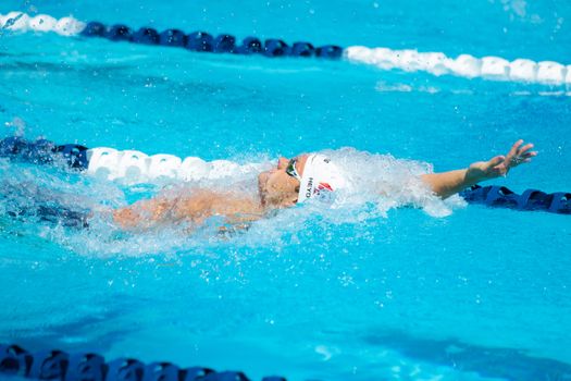 A swimmer in action performing the backstroke in a bright blue pool during a sunny day.
