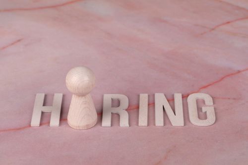 Free Wooden letters spelling 'hiring' on pink marble background with a peg. Stock Photo