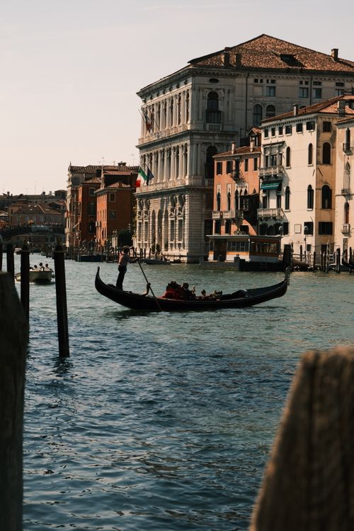 Free Gondola navigates the Grand Canal in Venice, Italy, with historical buildings and Italian flag in view. Stock Photo