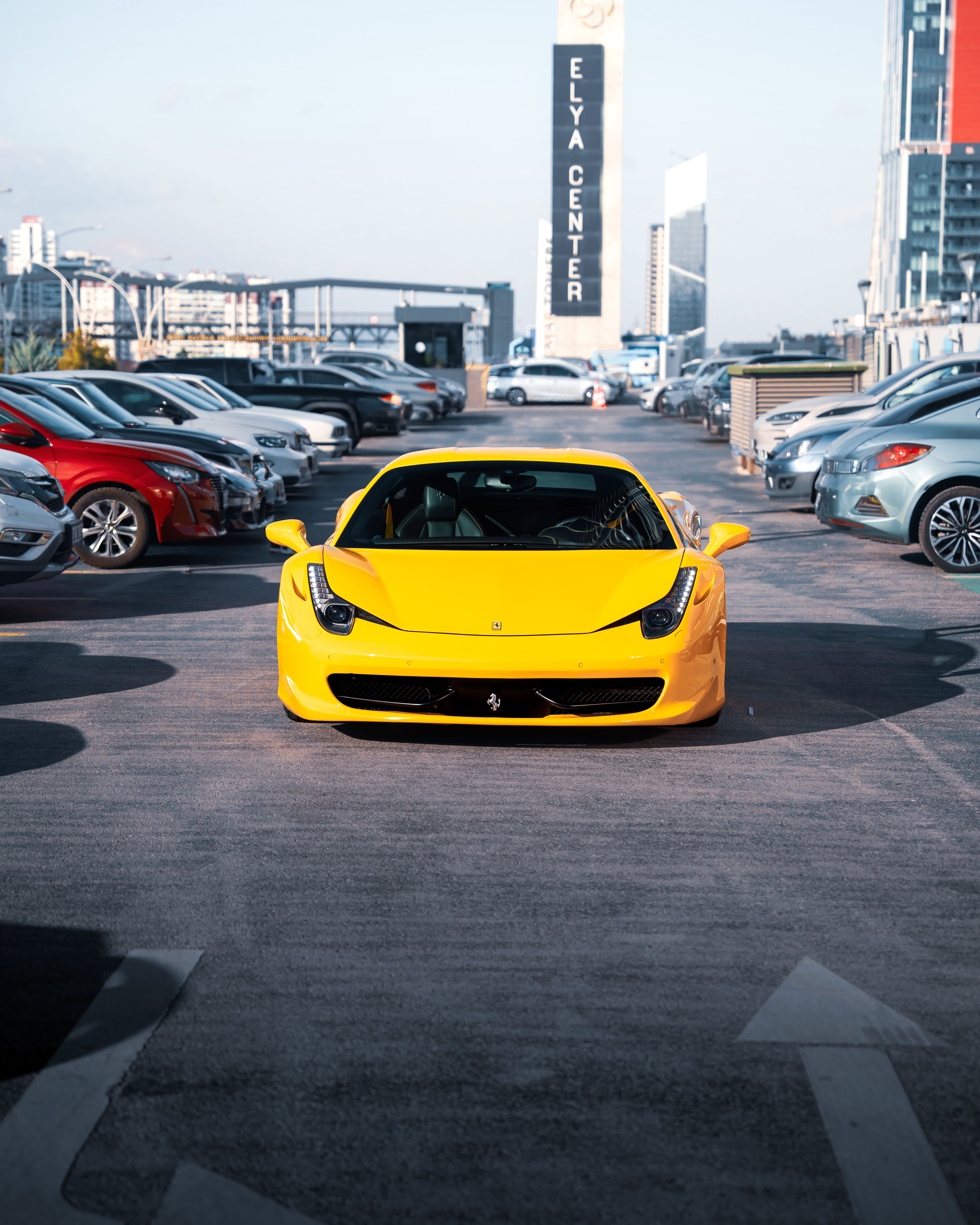 Bright yellow sports car prominently displayed in a bustling Ankara parking lot under clear skies.