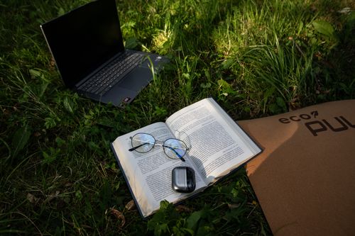 Free An open book, laptop, and glasses on grass symbolize a serene outdoor work environment. Stock Photo