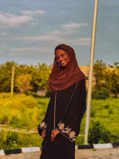 Free A woman in a brown hijab smiles warmly with a sunny outdoor backdrop. Stock Photo