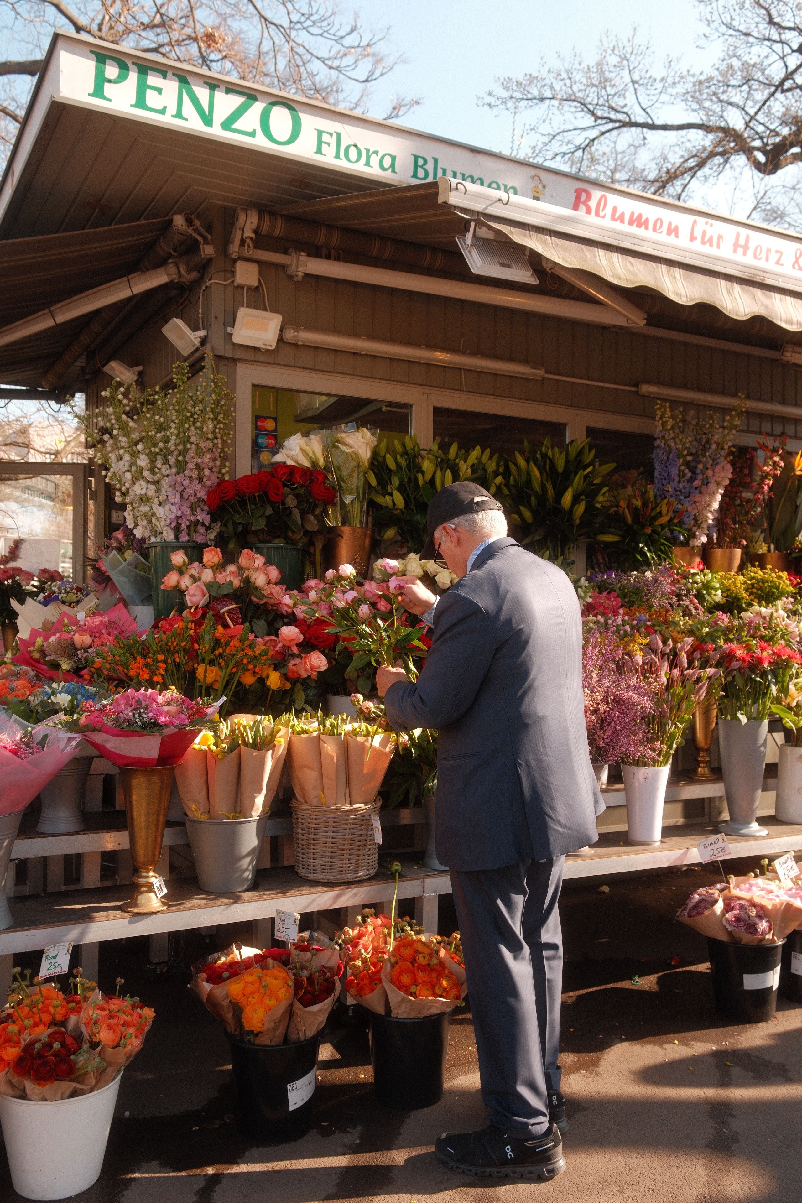 An elderly man browsing a vibrant flower stall in Vienna, Austria. Captures the charm of a traditional flower market.