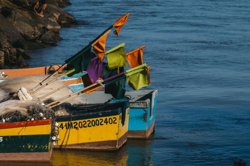 Free Fishing boats with colorful flags docked by a rocky shore on a clear day, showcasing vibrant detail. Stock Photo