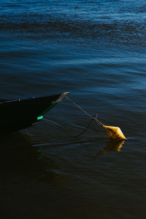 Free A peaceful scene of a boat with a yellow buoy floating on calm, deep blue water during the day. Stock Photo