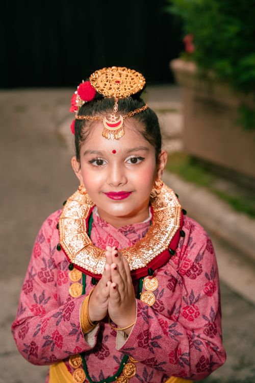 Free A young girl wearing vibrant traditional attire and jewelry performing a cultural gesture outdoors. Stock Photo