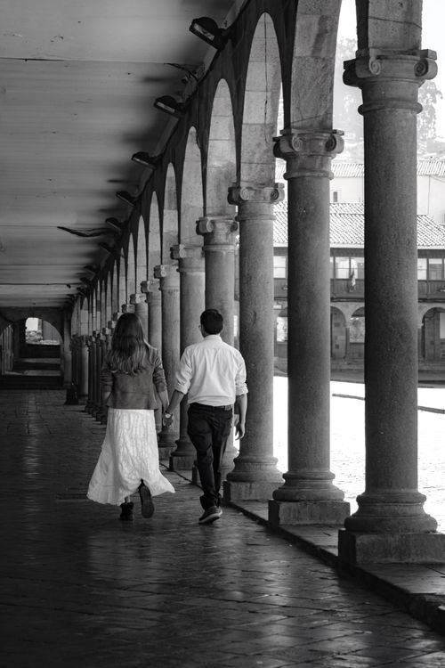 Free A couple walking hand in hand under a historic outdoor columned walkway. Stock Photo