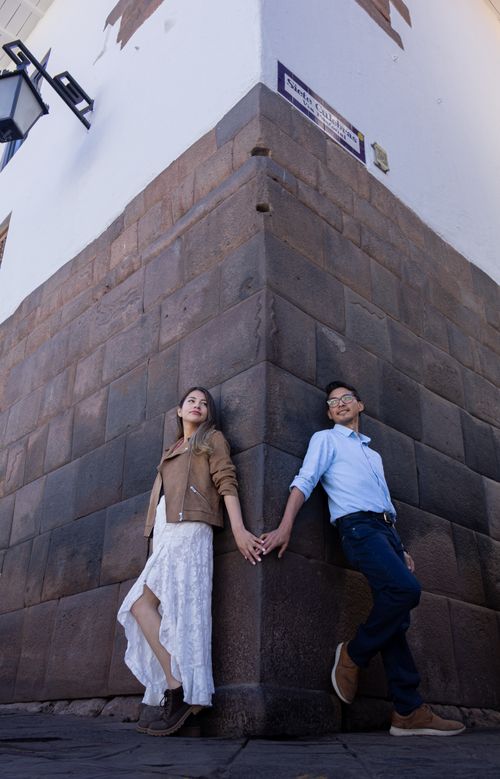 Free A stylish couple striking a pose against a historic stone wall corner outdoors. Stock Photo