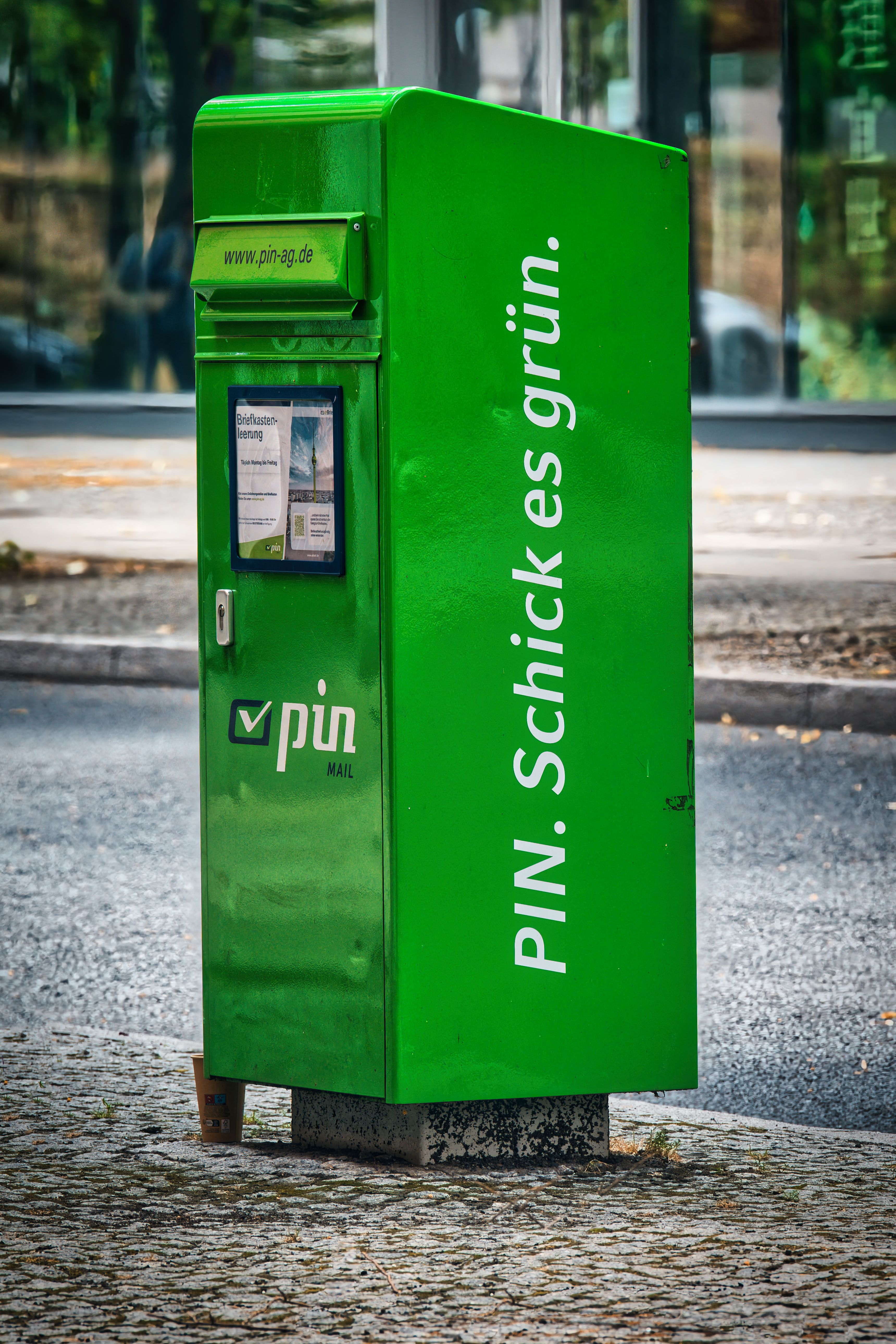 A green PIN postal mailbox stands on a Berlin street, encouraging eco-friendly mailing.