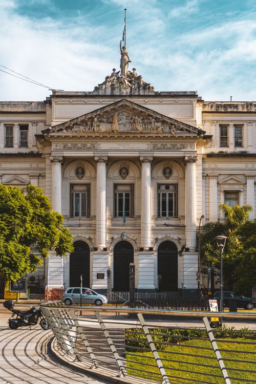 Free A neoclassical university building with grand columns and intricate sculptures under a clear blue sky. Stock Photo