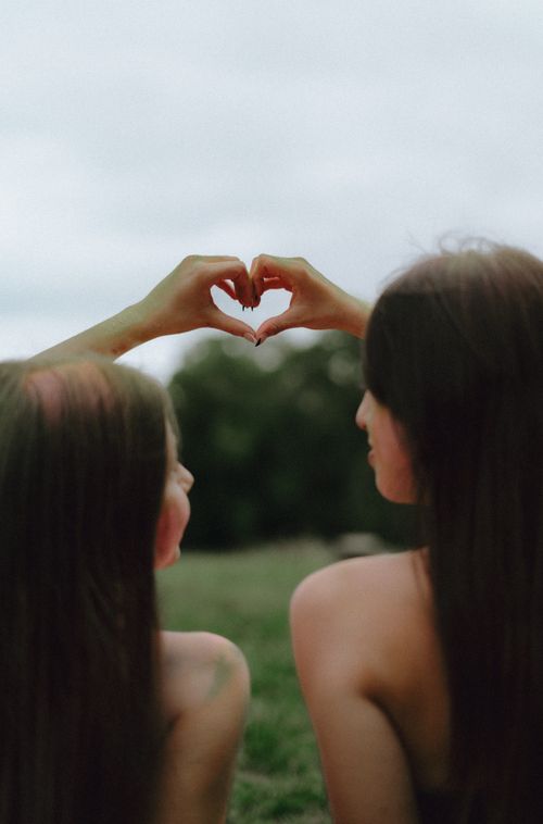 Free Two friends sit outdoors forming a heart shape with their hands, symbolizing friendship. Stock Photo