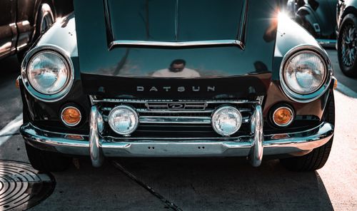 Free Close-up of a classic Datsun car front view with a visible human reflection in the chrome. Stock Photo