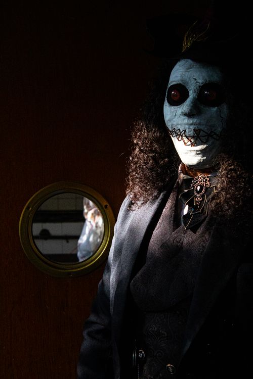 Free A mysterious figure in a dark costume with a creepy mask stands in a dimly lit room. Stock Photo